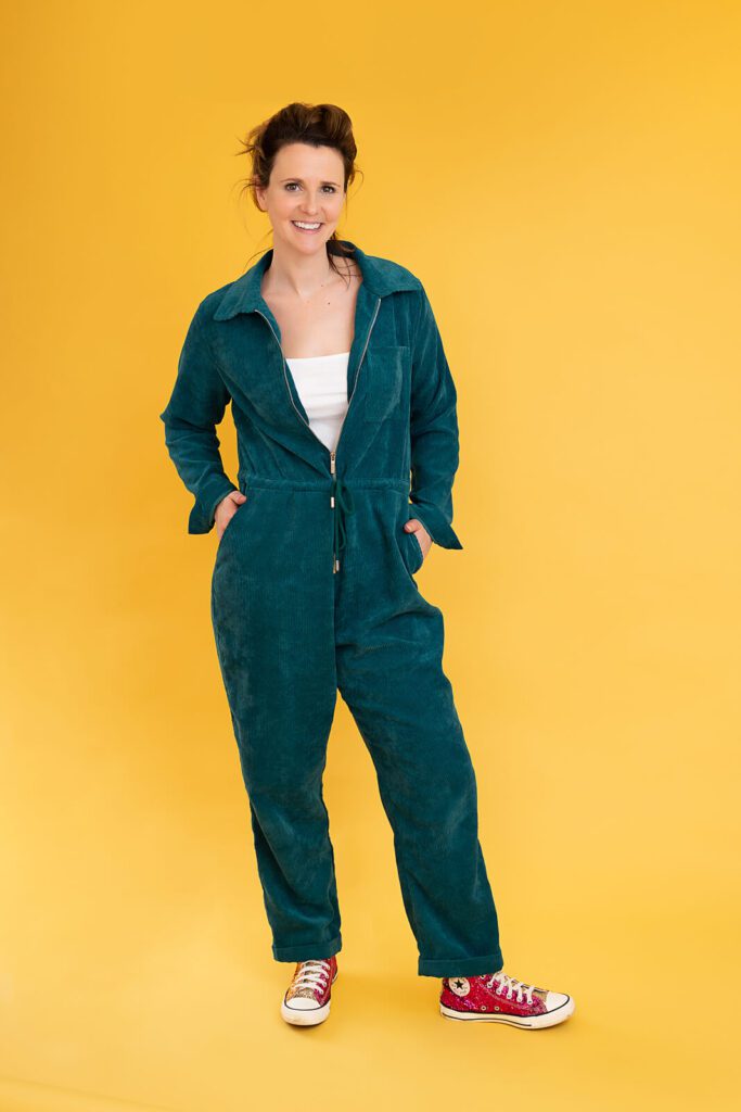Break The 4th Wall founder Jessica Haworth wearing a blue jumpsuit against a yellow background